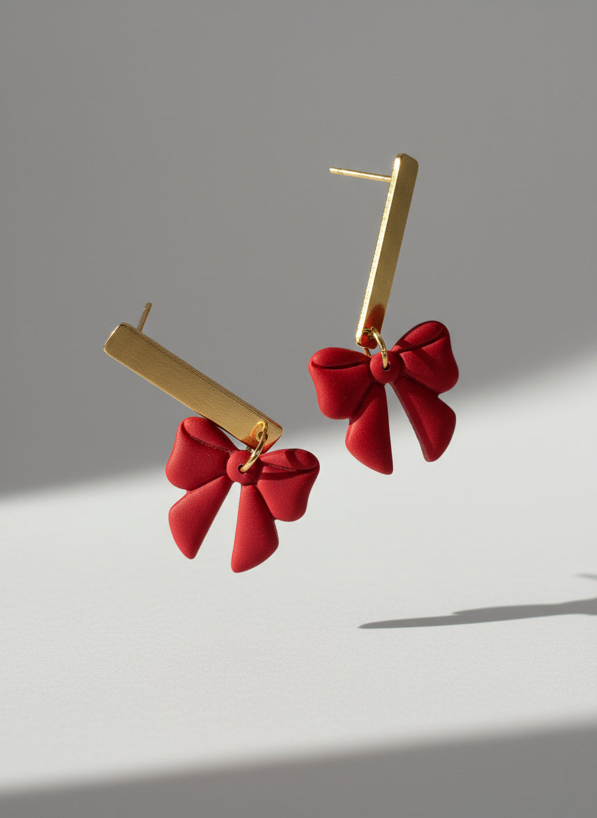 Red bow-shaped earrings with gold hooks on a white background